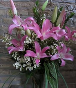 Pink lilies with greenery against brick wall.